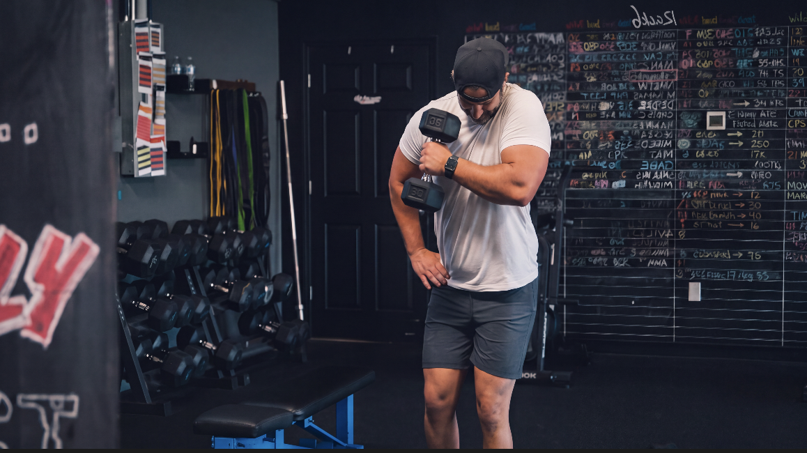 Member curling a dumbbell in front of the TitanUp PR chalkboard wall