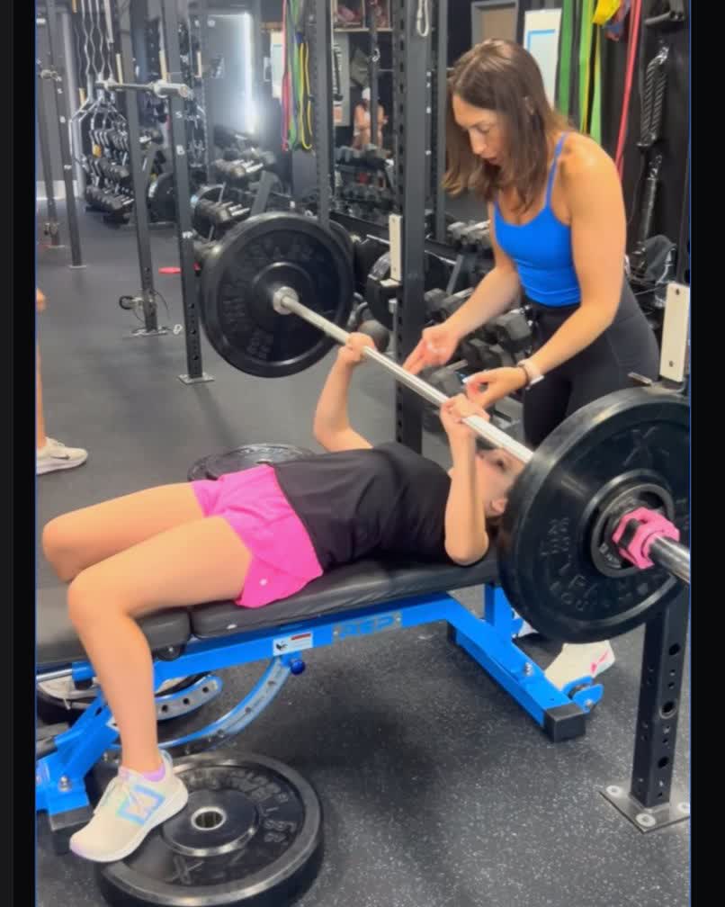 Young athlete bench pressing with coach spotting at TitanUp Nocatee