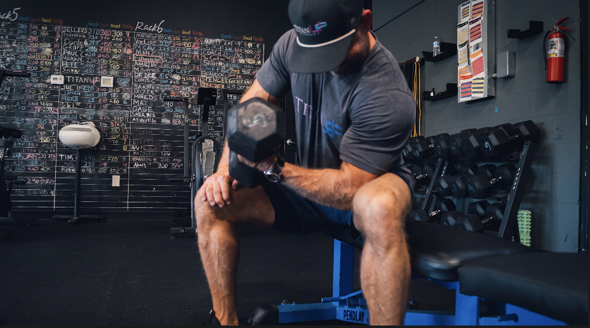 Member working a seated dumbbell curl beside the dumbbell rack