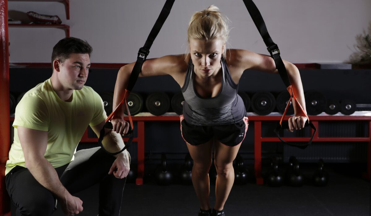 woman working out in gym with trainer looking on